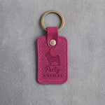 Fuchsia leather keychain debossed with a pug in a party hat and the words Party ANIMAL, on gray concrete