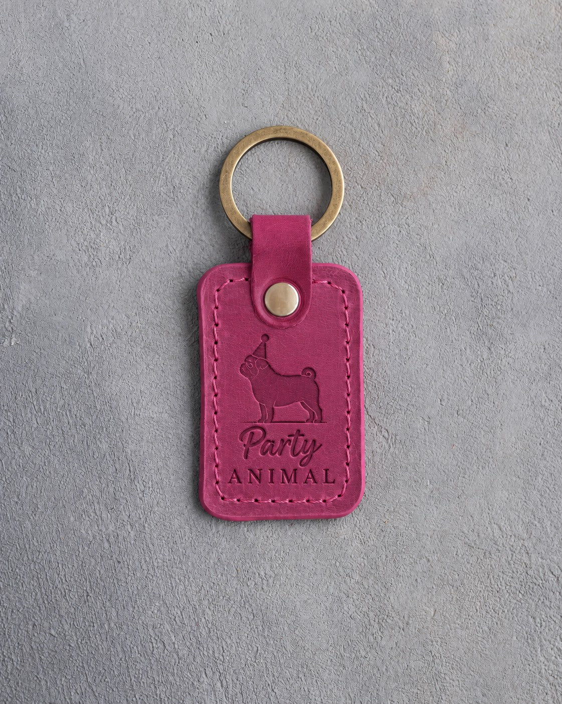 Fuchsia leather keychain debossed with a pug in a party hat and the words Party ANIMAL, on gray concrete