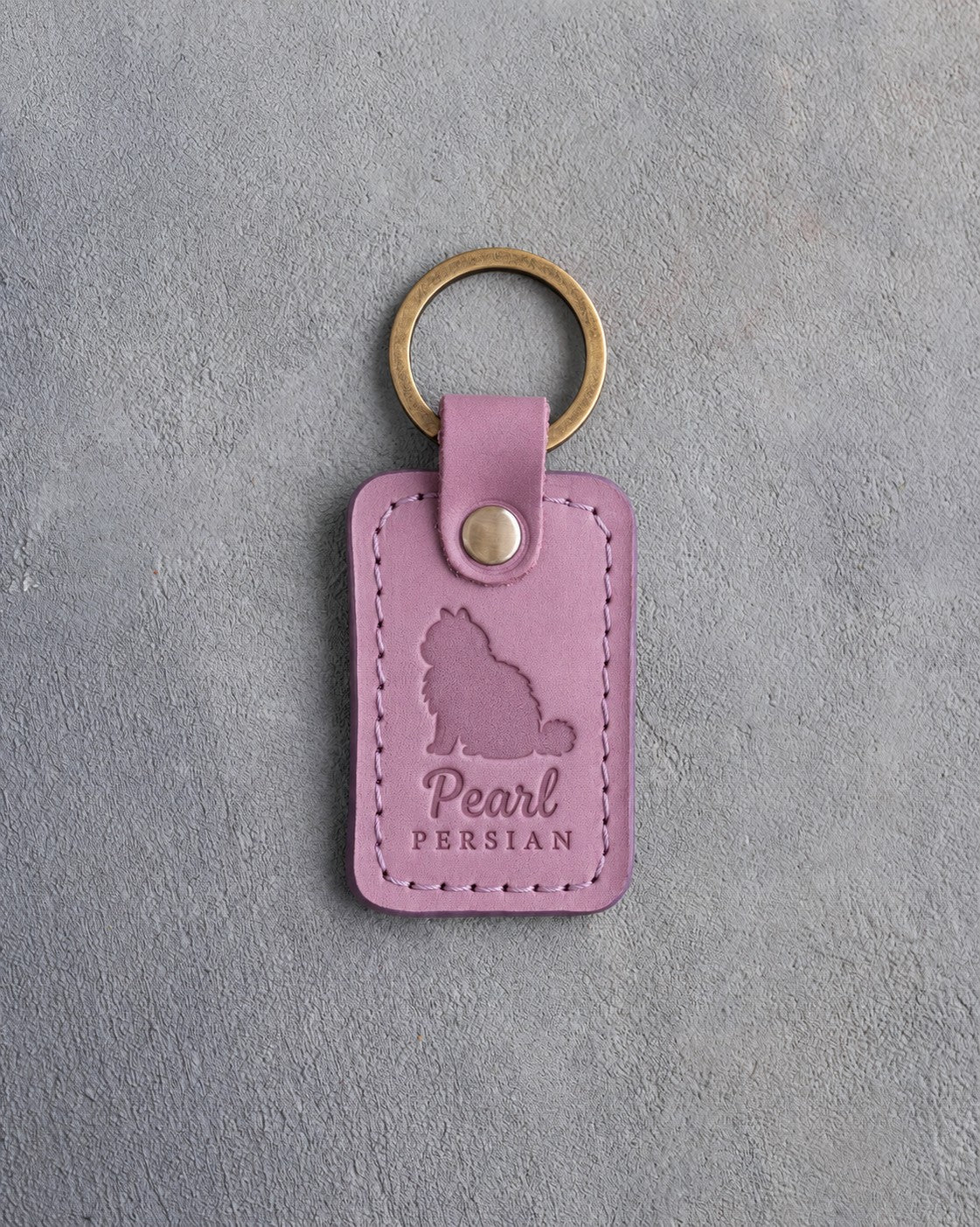 Lilac leather keychain debossed with a fluffy sitting Persian cat above the name Pearl and PERSIAN