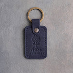 Blueberry navy leather keychain debossed with an aster above Aster and SEPTEMBER, on gray concrete