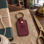 Wine red Eleanor's BOOK CLUB keychain on kraft paper beside a book half wrapped with cotton string