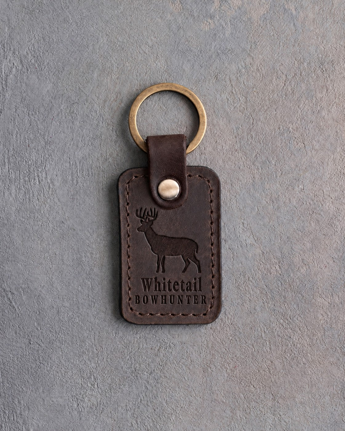 Dark espresso leather keychain debossed with a whitetail buck above the words Whitetail and BOWHUNTER, on gray concrete
