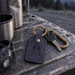 Navy Wade BULL ELK keychain clipped to a hunting pack strap against a granite boulder in the mountains