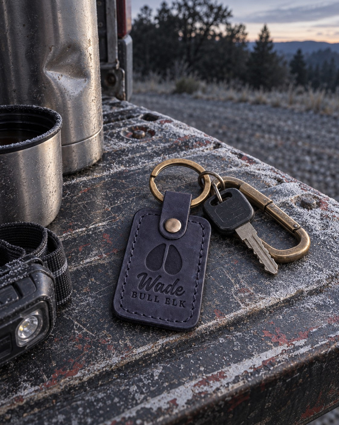 Navy Wade BULL ELK keychain clipped to a hunting pack strap against a granite boulder in the mountains