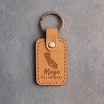 Indian Summer tan leather keychain debossed with a California silhouette and heart above the name Maya and CALIFORNIA, on gray concrete