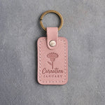 Blush pink leather keychain debossed with a carnation above Carnation and JANUARY, on gray concrete
