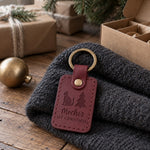 Mochi's 1ST CHRISTMAS keychain in wine red leather hanging from a Christmas tree branch