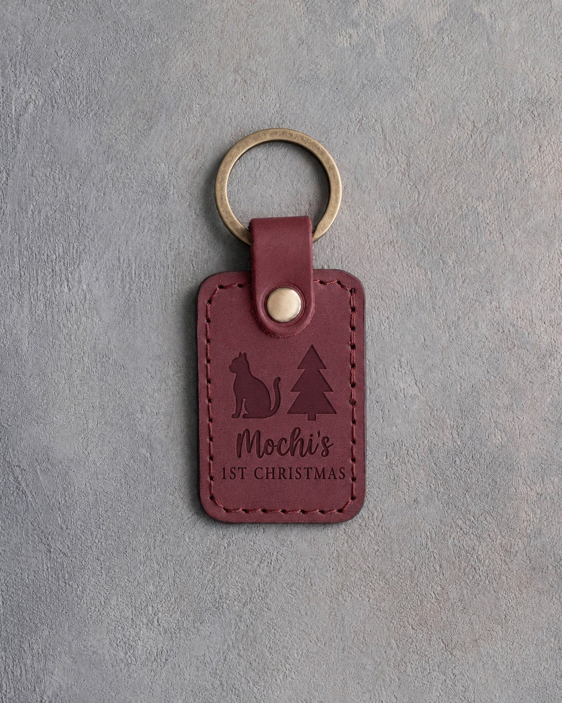 Sangria red leather keychain debossed with a small cat beside a Christmas tree above the name Mochi's and 1ST CHRISTMAS