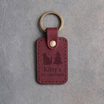 Sangria red leather keychain debossed with a small cat beside a Christmas tree above Kitty's and 1ST CHRISTMAS, on gray concrete