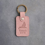 Blush pink leather keychain debossed with a cat on a windowsill above Kitty's and MOM, on gray concrete