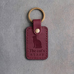 Sangria red leather keychain debossed with a cat looking up above The cat's and STAFF, on gray concrete