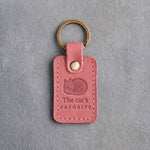 Parisian blossom pink leather keychain debossed with a curled sleeping cat above The cat's and FAVORITE, on gray concrete