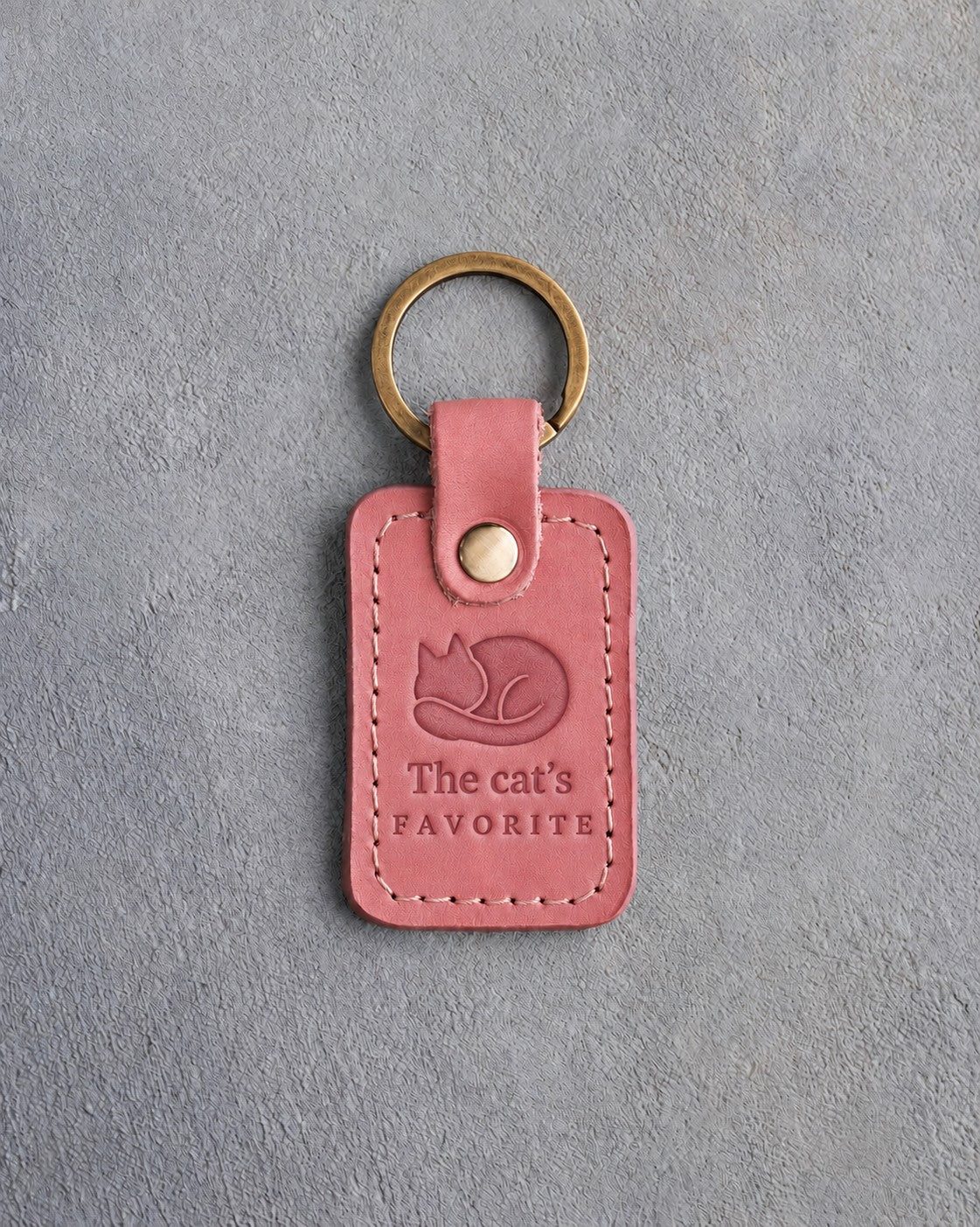 Parisian blossom pink leather keychain debossed with a curled sleeping cat above The cat's and FAVORITE, on gray concrete