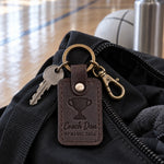 Dark brown Coach Dan keychain on a lanyard with gym keys beside a stack of orange cones