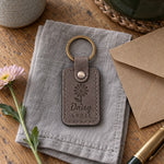 Gray Daisy April keychain on a wooden windowsill beside a jar of white garden daisies