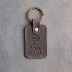 Country gray leather keychain debossed with a daisy above Daisy and APRIL, on gray concrete
