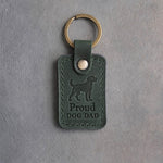 Forest green leather keychain debossed with an alert standing dog above Proud and DOG DAD, on gray concrete