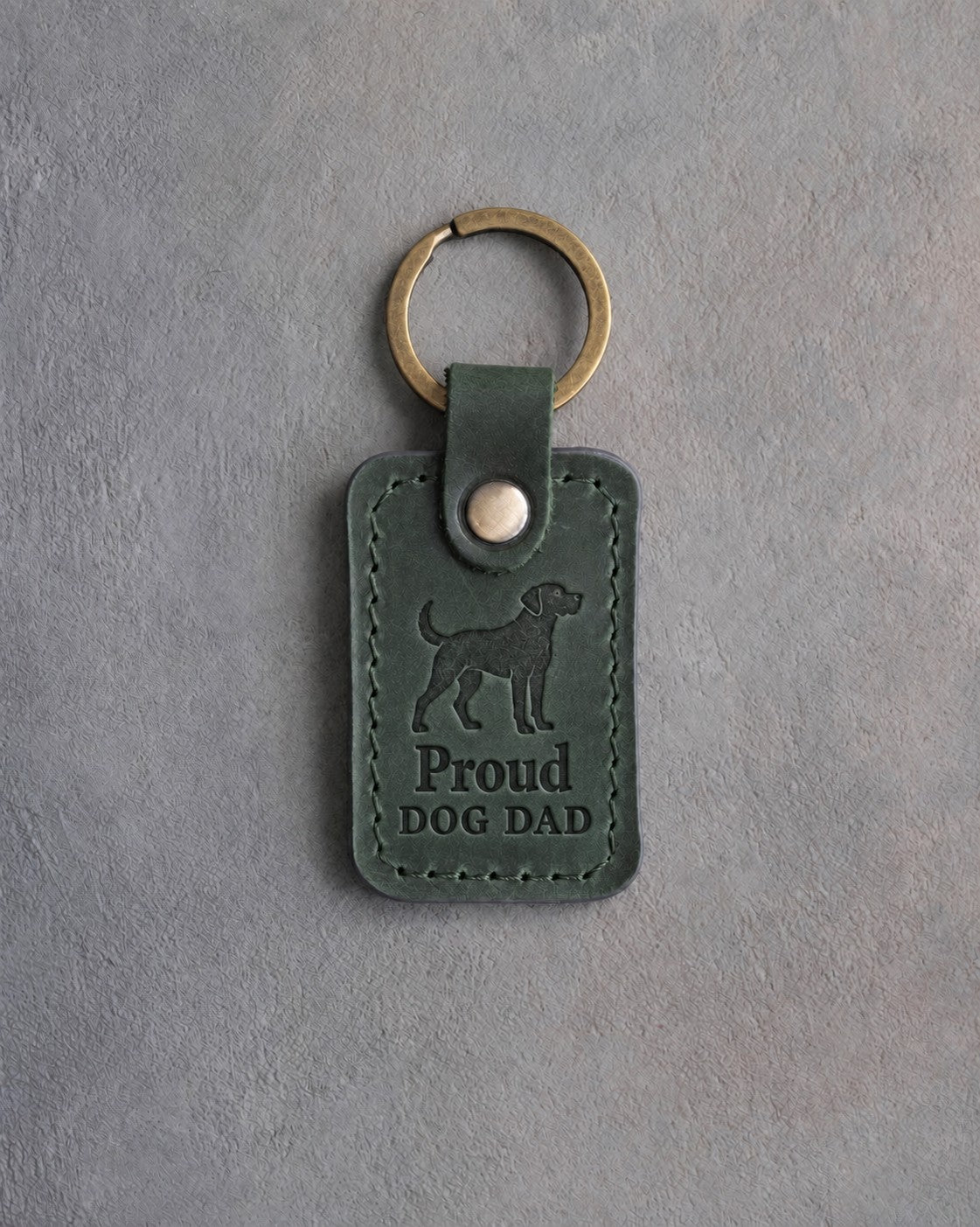 Forest green leather keychain debossed with an alert standing dog above Proud and DOG DAD, on gray concrete