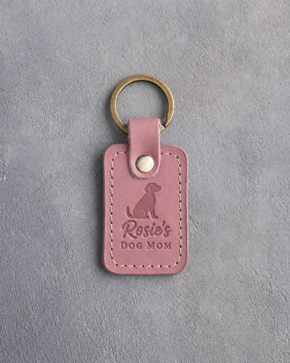 Parisian Blossom pink leather keychain debossed with a sitting dog above Rosie's and DOG MOM, on gray concrete