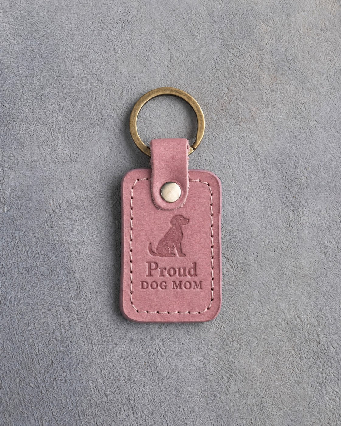 Parisian Blossom pink leather keychain debossed with a sitting dog above Proud and DOG MOM, on gray concrete