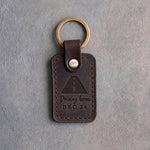 Dark espresso leather keychain debossed with an open road in perspective above Driving home and DEC 24, on gray concrete