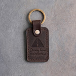 Dark espresso leather keychain debossed with an open road in perspective above the words Driving home and FOR CHRISTMAS, on gray concrete