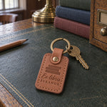 Caramel Ex libris ELEANOR keychain resting on an open hardcover beside a green reading lamp