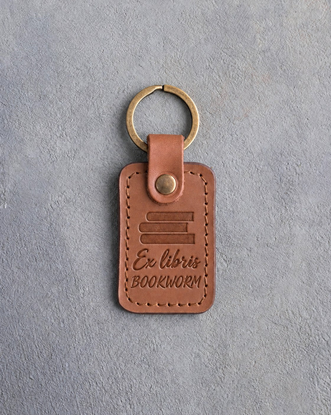 Caramel leather keychain debossed with a stack of books above Ex libris and BOOKWORM, on gray concrete