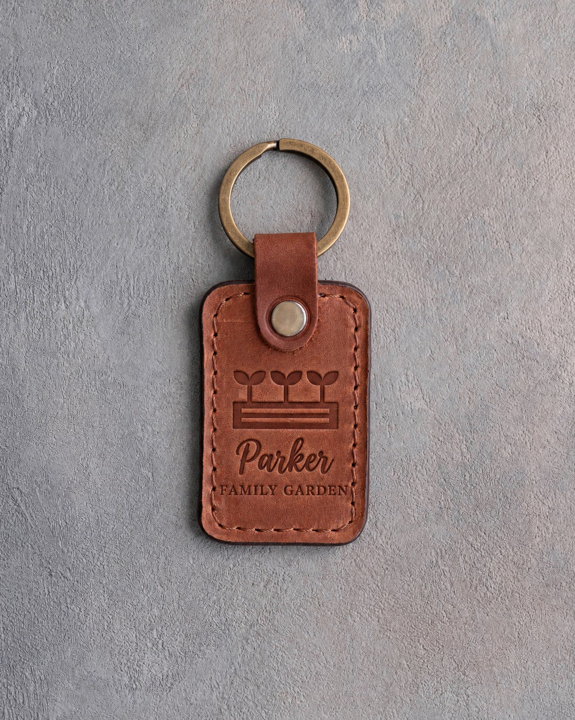 Arizona tan leather keychain debossed with a raised garden bed of seedlings above Parker and FAMILY GARDEN, on gray concrete