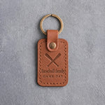 Caramel leather keychain debossed with two crossed bats above the words Baseball family and GAME DAY, on gray concrete