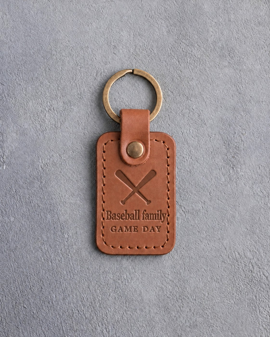 Caramel leather keychain debossed with two crossed bats above the words Baseball family and GAME DAY, on gray concrete