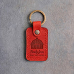 Poppy red leather keychain debossed with a gambrel barn above the words Family farm and BORN AND RAISED, on gray concrete