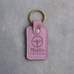 Lilac leather keychain debossed with a steering wheel above Maddie's and FIRST CAR