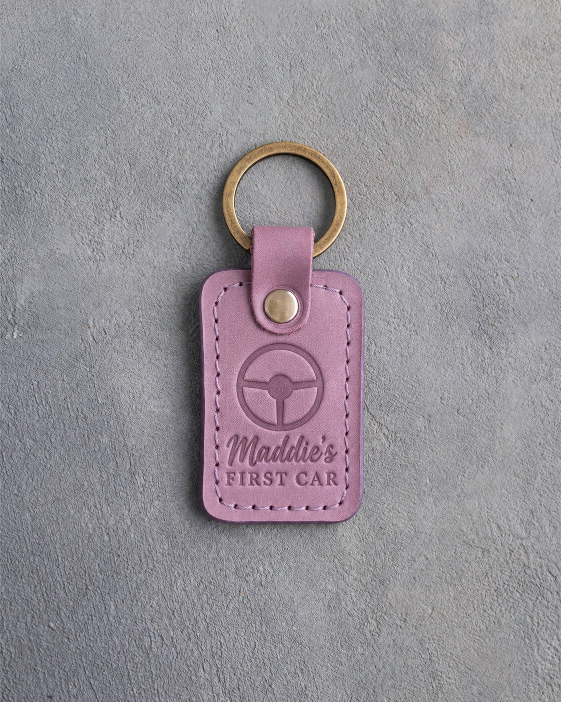 Lilac leather keychain debossed with a steering wheel above Maddie's and FIRST CAR