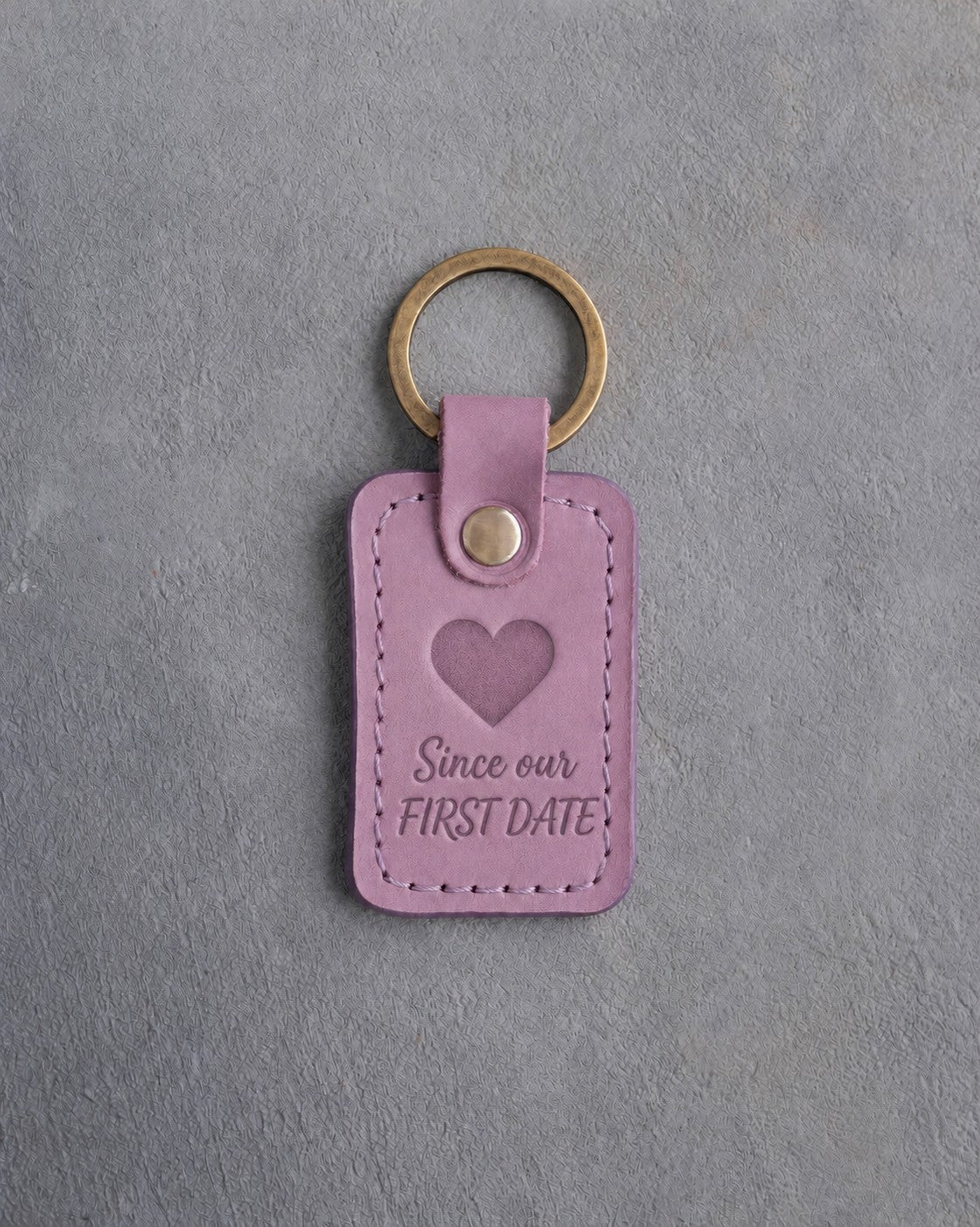 Lilac leather keychain debossed with a solid heart above the words Since our and FIRST DATE, on gray concrete