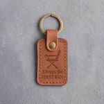 Caramel leather keychain debossed with a folding sideline chair above Always the and FIRST FAN, on gray concrete