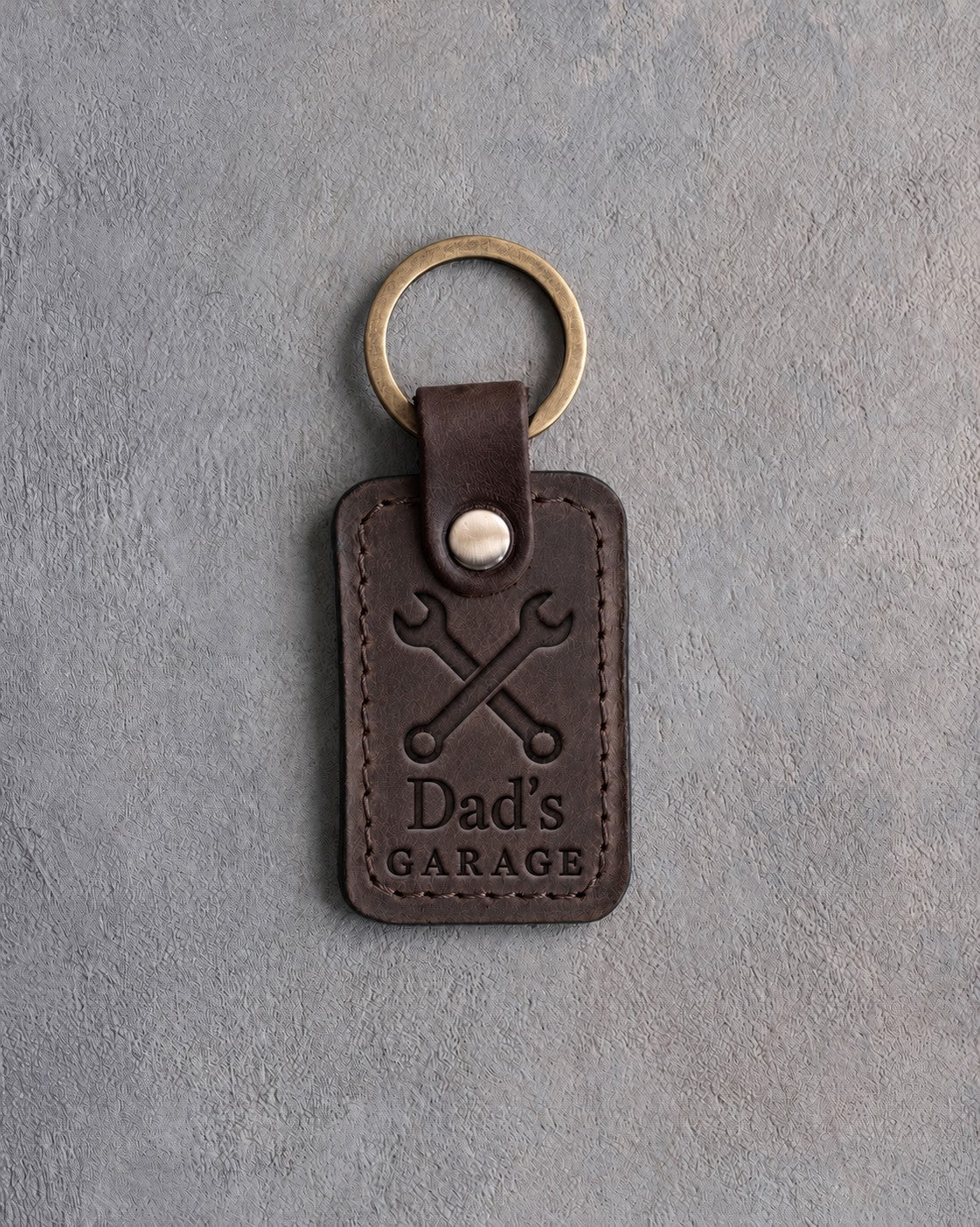 Dark espresso leather keychain debossed with crossed wrenches above the words Dad's and GARAGE, on gray concrete