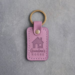 Lilac leather keychain debossed with a gable-front house above Grandma's and HOUSE, on gray concrete