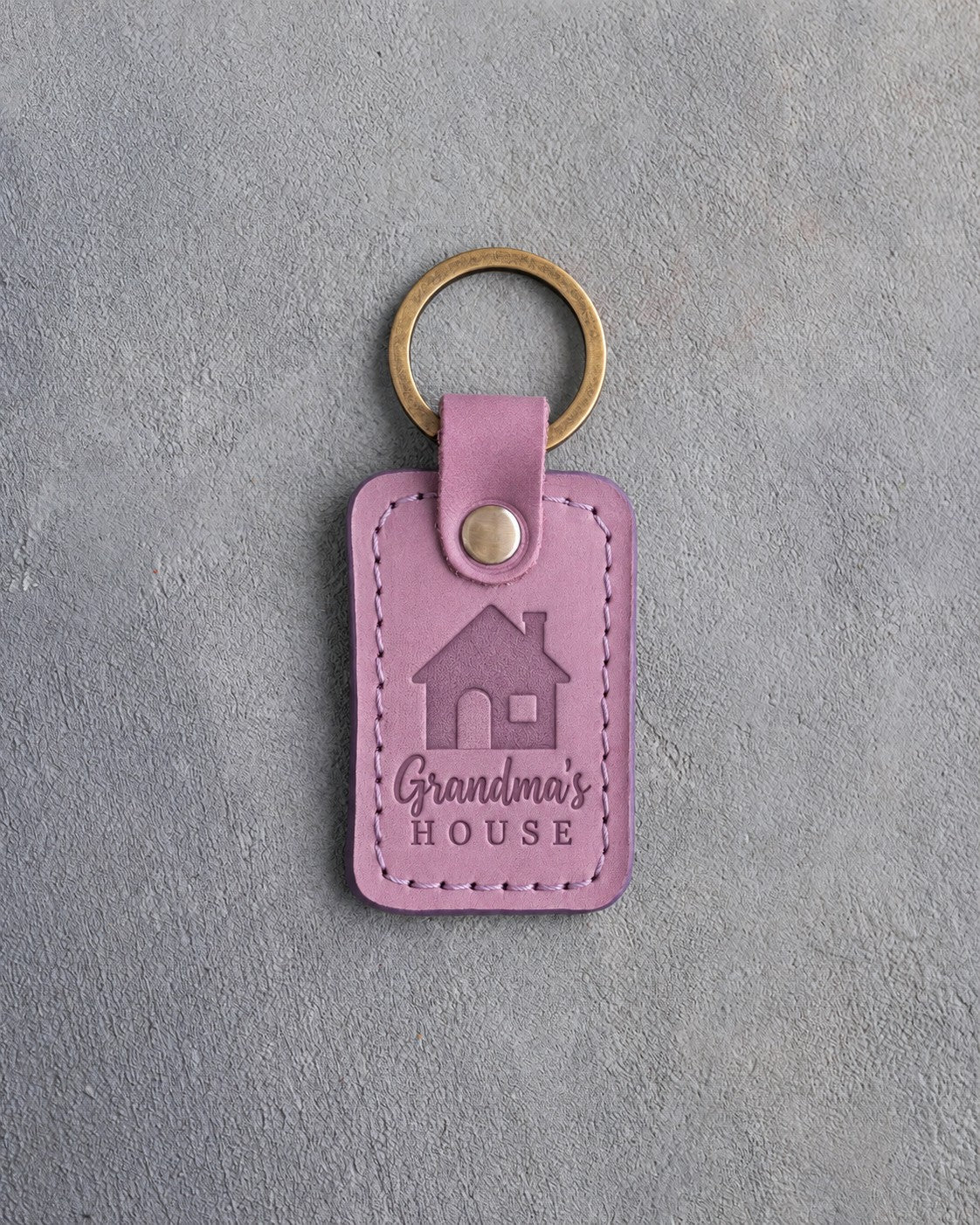 Lilac leather keychain debossed with a gable-front house above Grandma's and HOUSE, on gray concrete