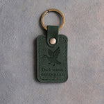 Forest green leather keychain debossed with a mallard cupped to land above the words Duck season and GREENHEAD, on gray concrete