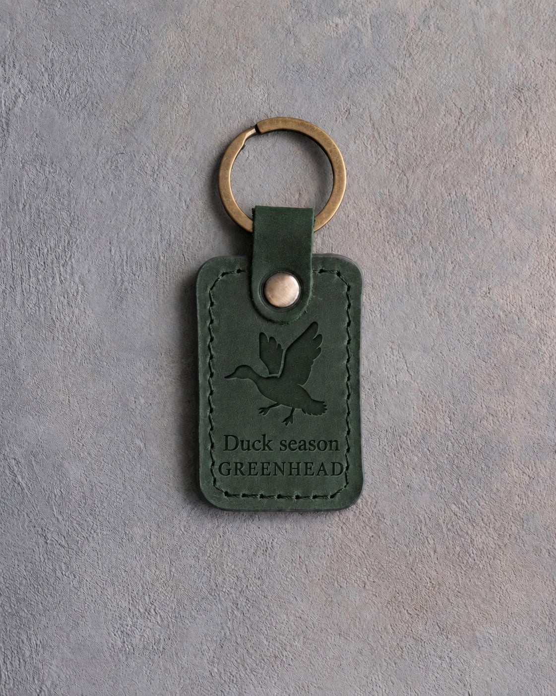 Forest green leather keychain debossed with a mallard cupped to land above the words Duck season and GREENHEAD, on gray concrete