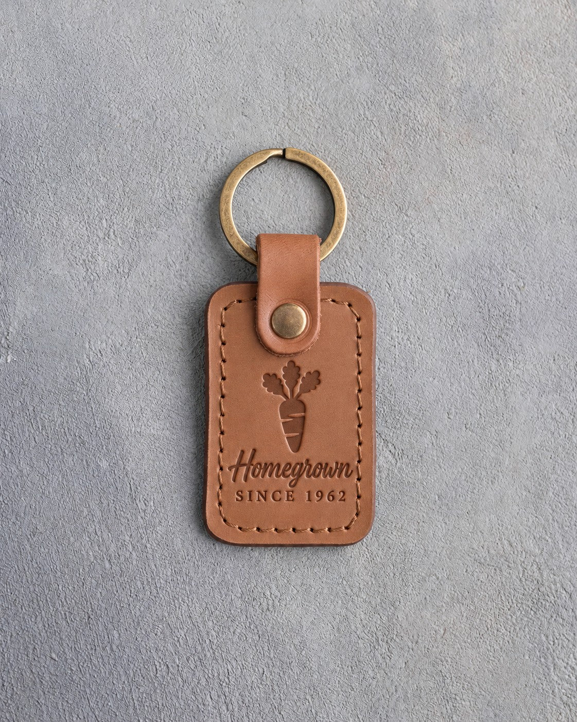 Caramel leather keychain debossed with a carrot above Homegrown and SINCE 1962, on gray concrete
