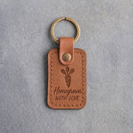 Caramel leather keychain debossed with a carrot above Homegrown and WITH LOVE, on gray concrete