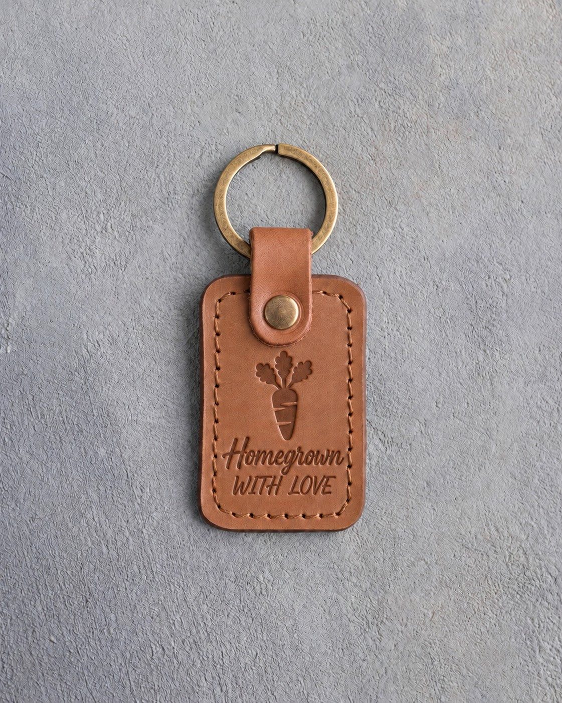 Caramel leather keychain debossed with a carrot above Homegrown and WITH LOVE, on gray concrete