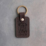 Dark espresso leather keychain debossed with a jersey numbered 17 above the name Lily's and DAD, on gray plaster