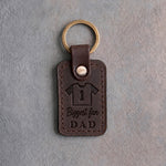 Dark espresso leather keychain debossed with a jersey numbered 1 above the words Biggest fan and DAD, on gray concrete