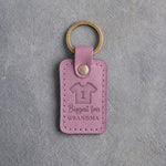 Lilac leather keychain debossed with a jersey numbered 1 above the words Biggest fan and GRANDMA, on gray concrete