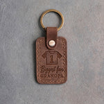 Sicilian brown leather keychain debossed with a jersey numbered 1 above the words Biggest fan and GRANDPA, on gray concrete