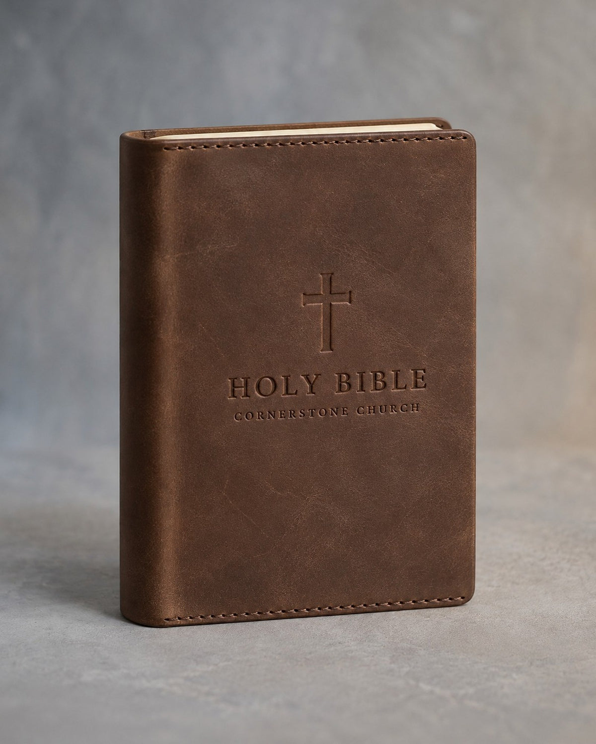 Sicilian Brown slip-on leather Bible cover debossed with a cross, HOLY BIBLE and a sample church name, on grey plaster