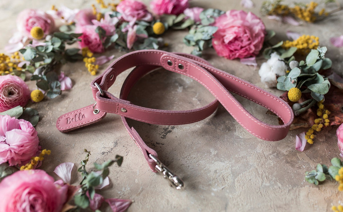 Personalized pink leather dog leash with a cursive name tab among flowers